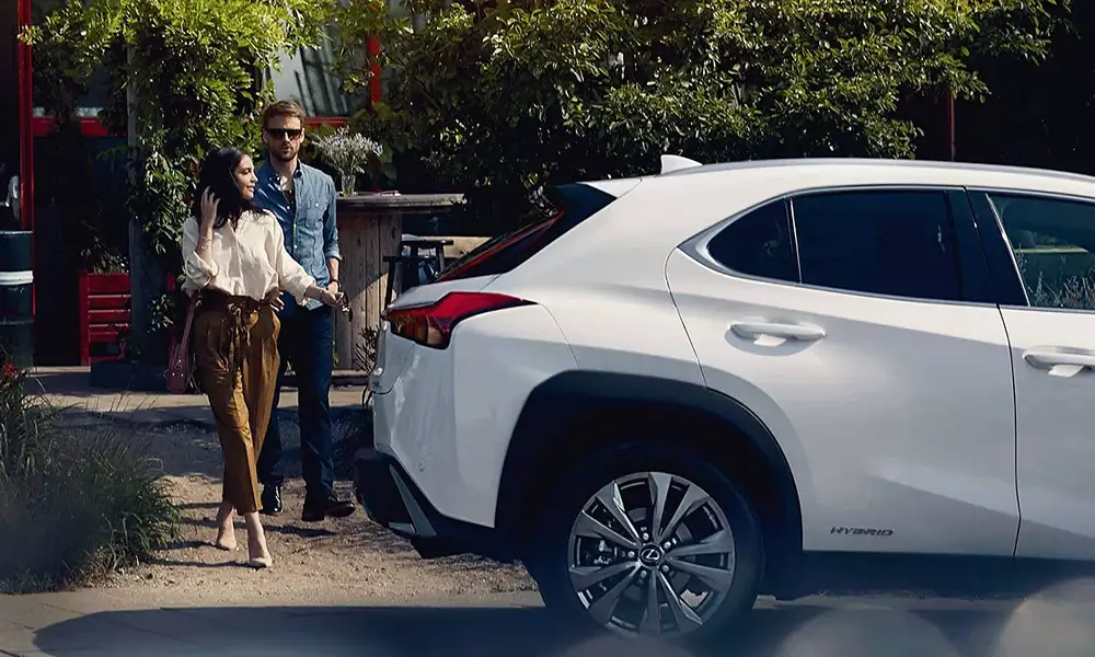 Elegancka para przy białym samochodzie hybrydowym marki Lexus.